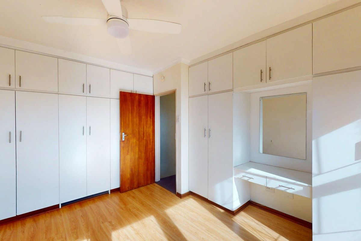 A bright bedroom featuring extensive built-in cabinetry, a vanity area with a mirror, a ceiling fan, and light-toned laminate flooring.