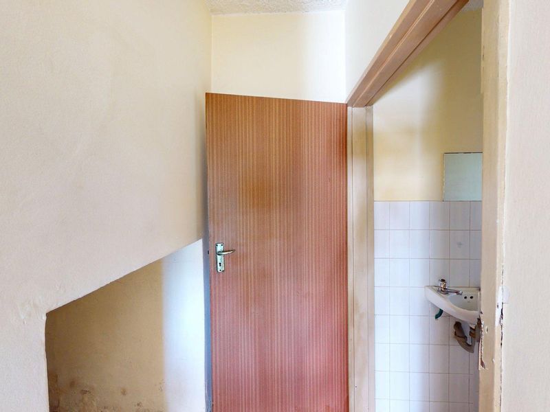 A small, dated bathroom featuring a wall-mounted basin with tiled splashback, requiring cosmetic updates and repairs to wall surfaces and plumbing fixtures.