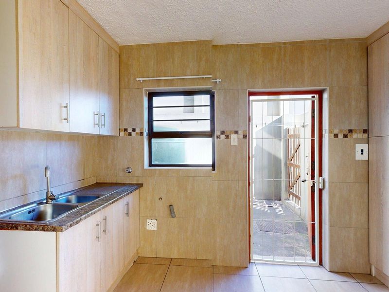 A functional kitchen featuring built-in cabinetry, tiled finishes, and direct access to an exterior area through a security gate.