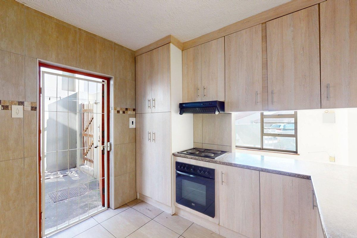 A functional kitchen featuring light wood-finish cabinetry, built-in oven and hob, tiled walls, and direct access to an outdoor area via a security gate.