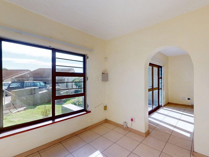 An empty living area featuring tiled floors, an arched entryway, and large windows providing natural light and views of the exterior.
