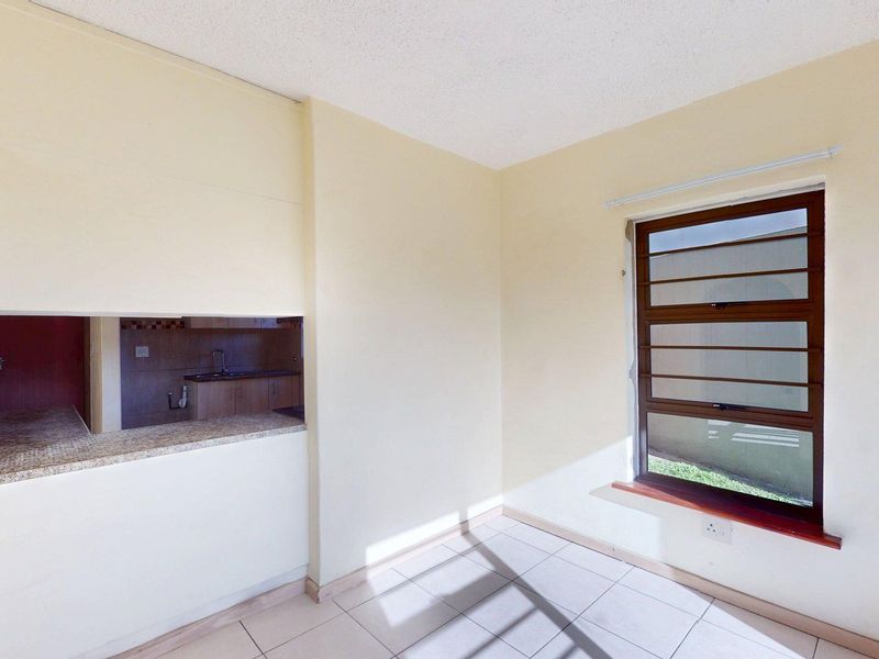 An empty open-plan living area featuring tiled flooring, a granite breakfast counter overlooking the kitchen, and a large louvre window.