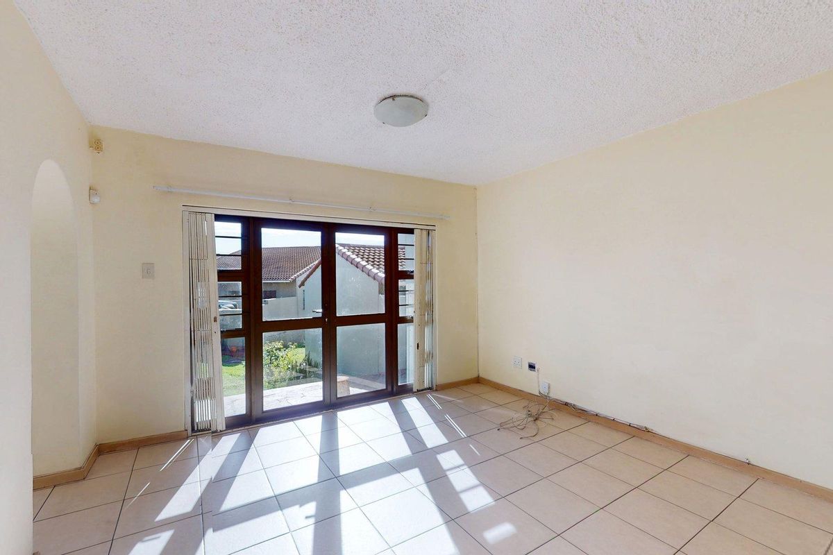 An empty living room featuring tiled flooring, a textured ceiling, and a sliding glass door providing access to the exterior.