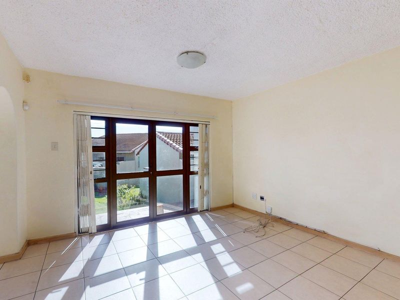 An empty living room featuring tiled flooring, a textured ceiling, and a sliding glass door providing access to the exterior.