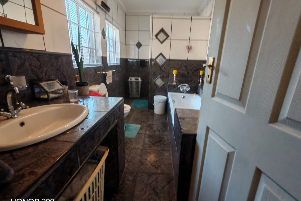 A dated bathroom featuring dark tiled surfaces, a built-in vanity with a ceramic basin, and a standard bathtub.