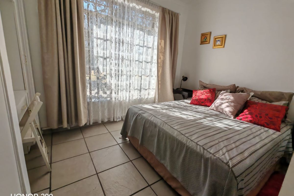 A functional bedroom featuring tiled flooring and large windows with installed curtain rails, providing natural light.