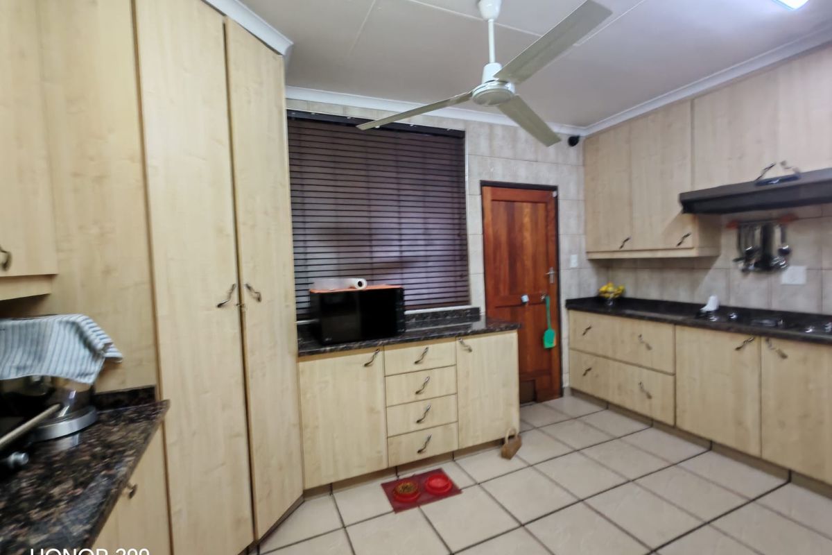 A functional kitchen featuring light wood-tone cabinetry, granite countertops, tiled flooring, and a ceiling fan, offering a practical layout for daily meal preparation.