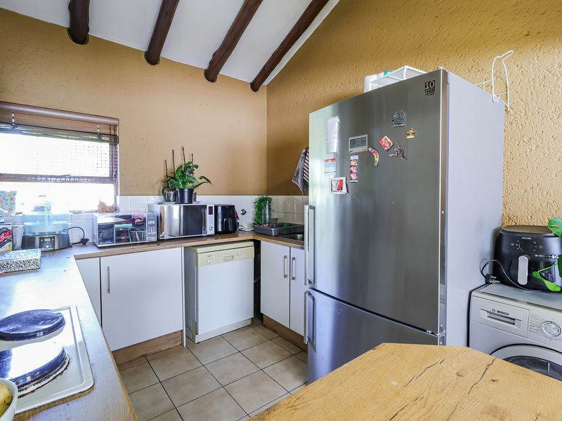 A functional kitchen featuring tiled flooring, exposed timber ceiling beams, built-in cabinetry, and a tiled backsplash.