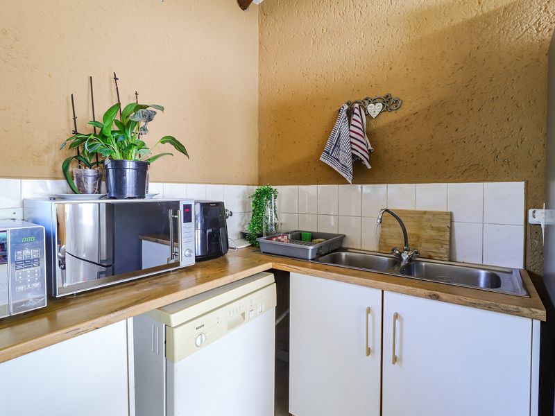 A compact kitchen area featuring a double bowl stainless steel sink, tiled splashback, and laminate countertops with built-in cabinetry.