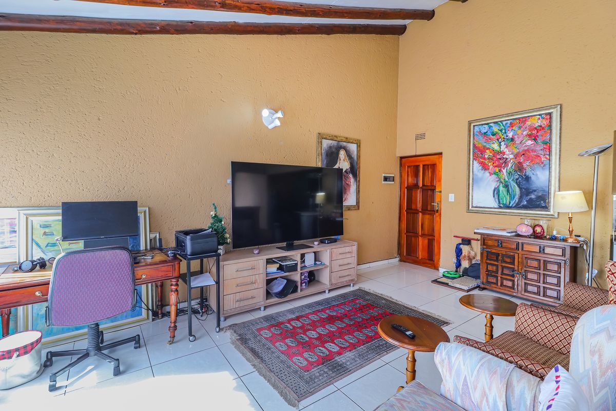 A spacious living room featuring exposed timber ceiling beams, tiled flooring, and a solid timber door, offering a warm and traditional aesthetic.