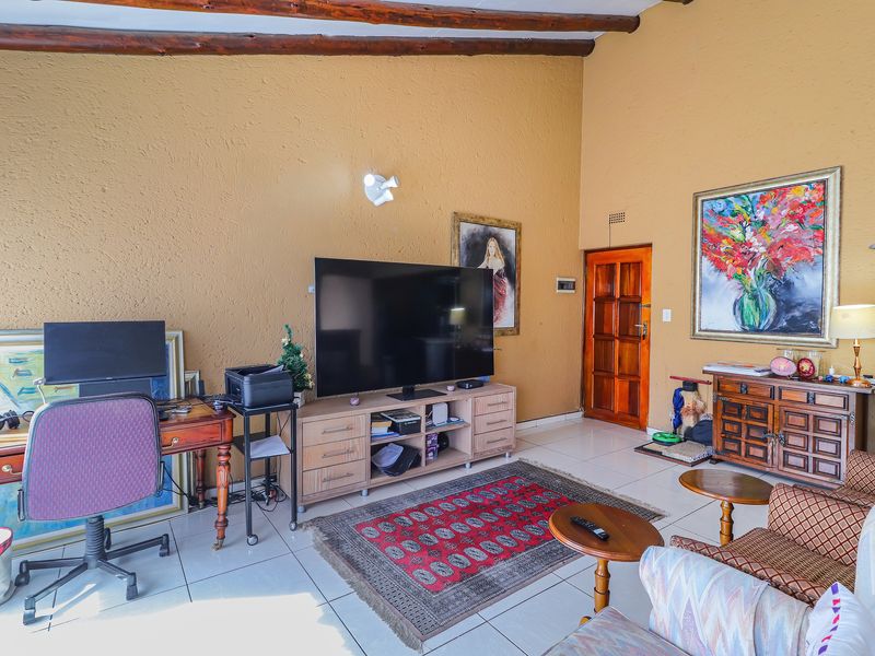 A spacious living room featuring exposed timber ceiling beams, tiled flooring, and a solid timber door, offering a warm and traditional aesthetic.