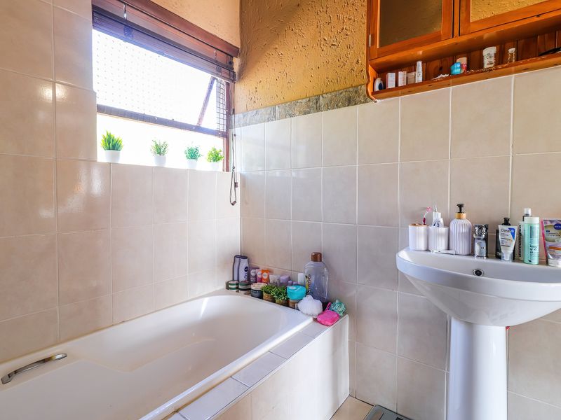 A functional bathroom featuring a built-in bathtub, pedestal sink, and wall-mounted wooden storage cabinet with tiled wall finishes.