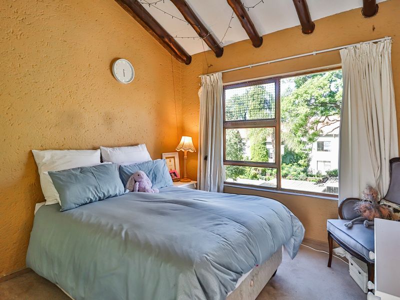 A bedroom featuring exposed timber ceiling beams, textured walls, and a large window providing natural light and garden views.