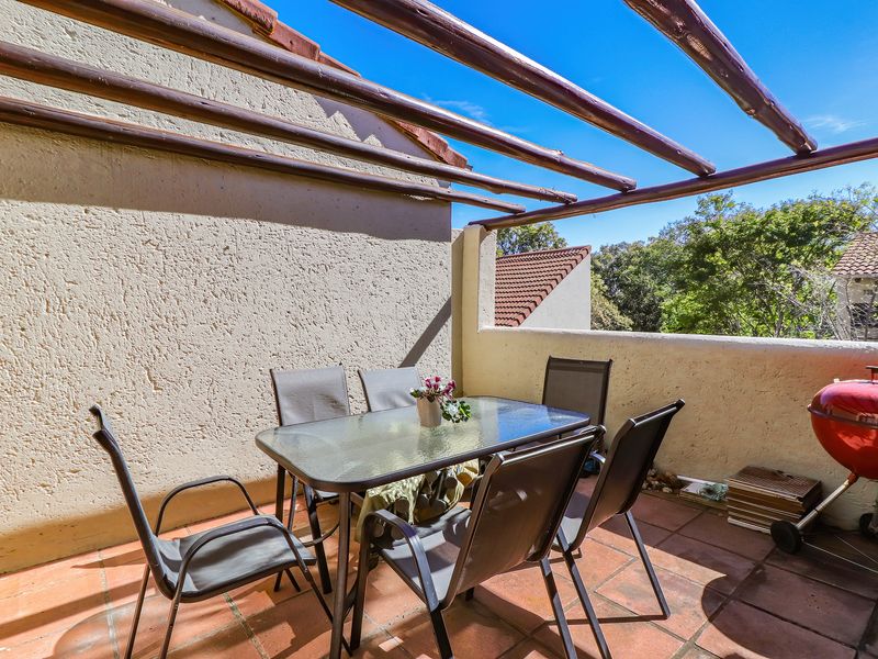A private balcony featuring terracotta floor tiles and a timber pergola, offering an open-air space suitable for outdoor dining.