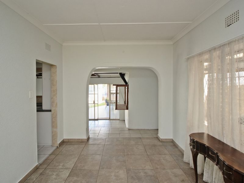 A bright, open-plan living area featuring neutral tiled flooring, a classic archway transition, and direct access to the rear patio through sliding glass doors.