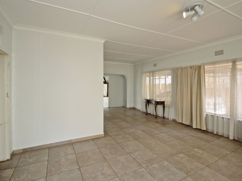 Spacious, light-filled living area featuring neutral tiled flooring, a classic archway transition, and large windows with ample natural light.
