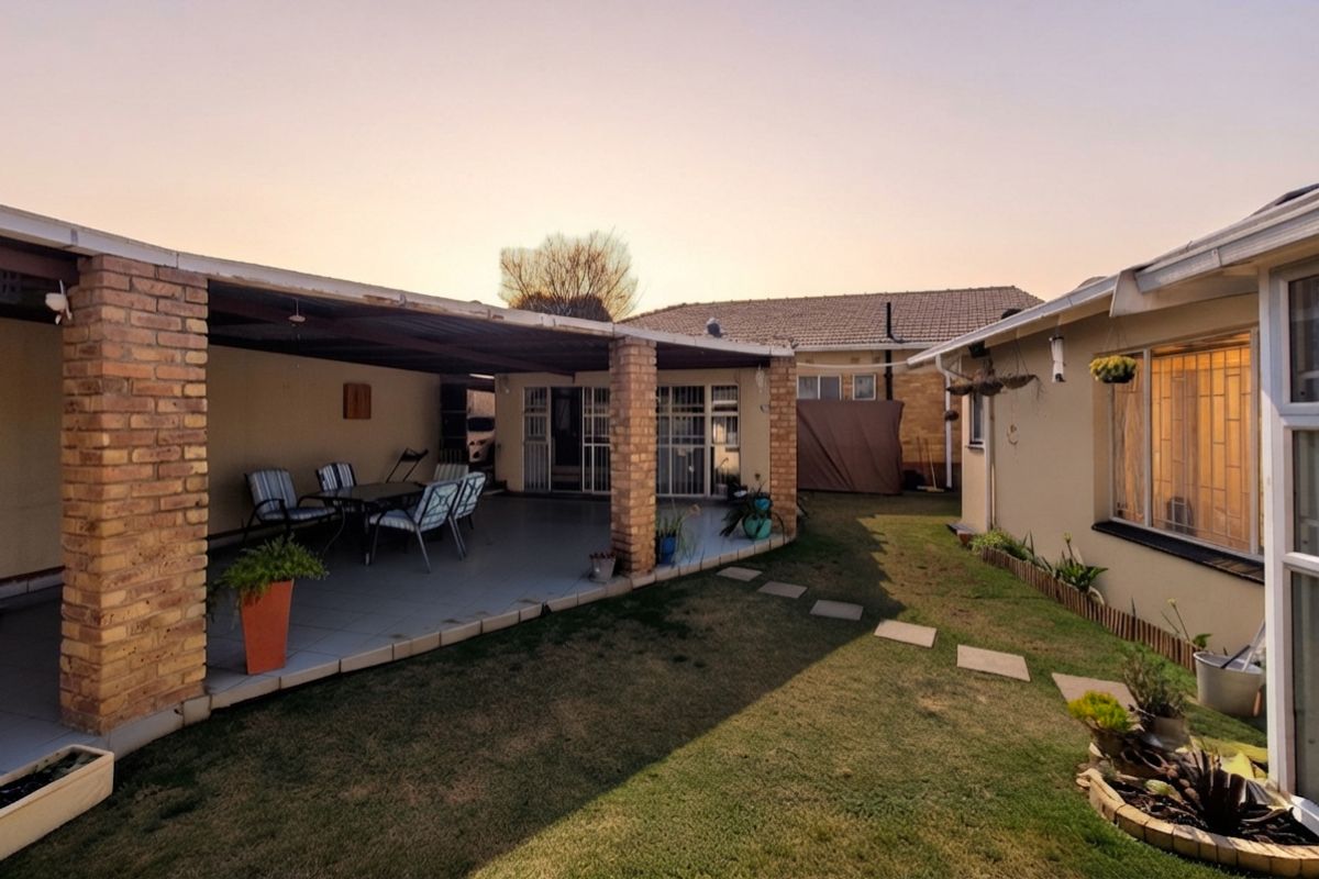 A rear view of the property featuring a covered brick-pillar patio, tiled flooring, and a well-maintained lawn with a garden path.