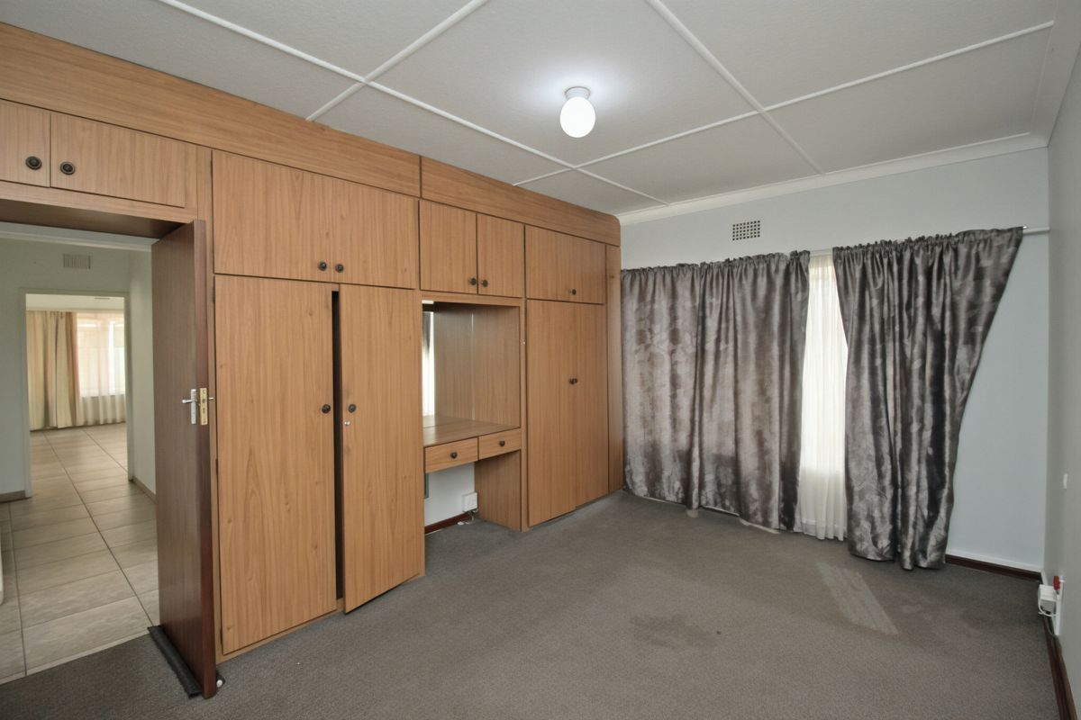 A spacious bedroom featuring extensive built-in wooden cupboards with an integrated vanity, carpeted flooring, and a tiled ceiling.