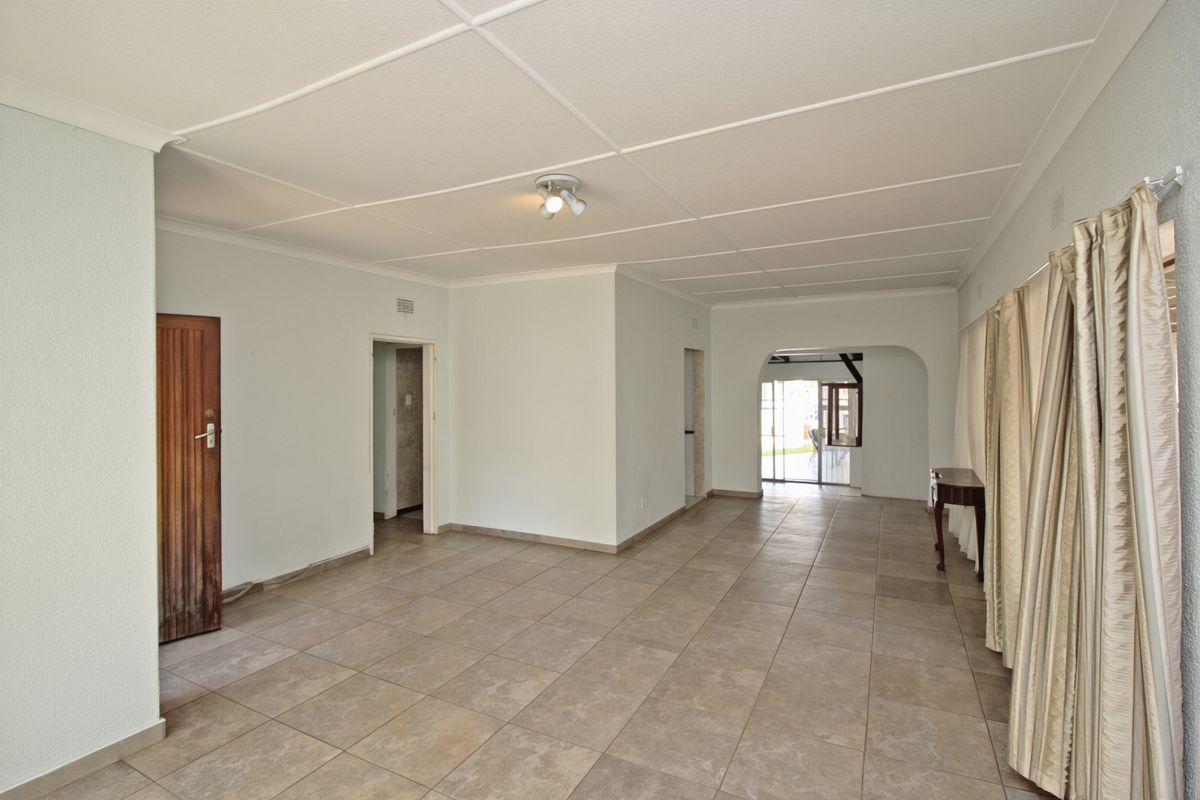 A spacious, empty living area featuring neutral tiled flooring, a classic archway leading to an adjacent space, and a traditional tiled ceiling.