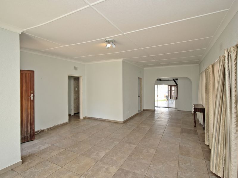 A spacious, empty living area featuring neutral tiled flooring, a classic archway leading to an adjacent space, and a traditional tiled ceiling.