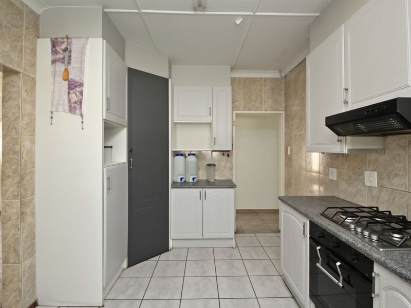 A functional kitchen featuring white cabinetry, gas hob, built-in oven, extractor fan, and tiled splashbacks with neutral floor tiles.