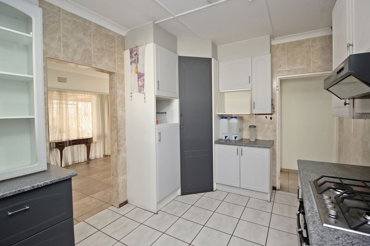 A functional kitchen featuring built-in cabinetry, a gas hob with extractor fan, and tiled finishes, offering a clean space ready for modern updates.