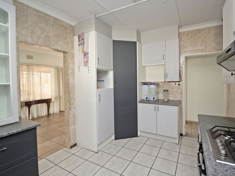 A functional kitchen featuring built-in cabinetry, a gas hob with extractor fan, and tiled finishes, offering a clean space ready for modern updates.