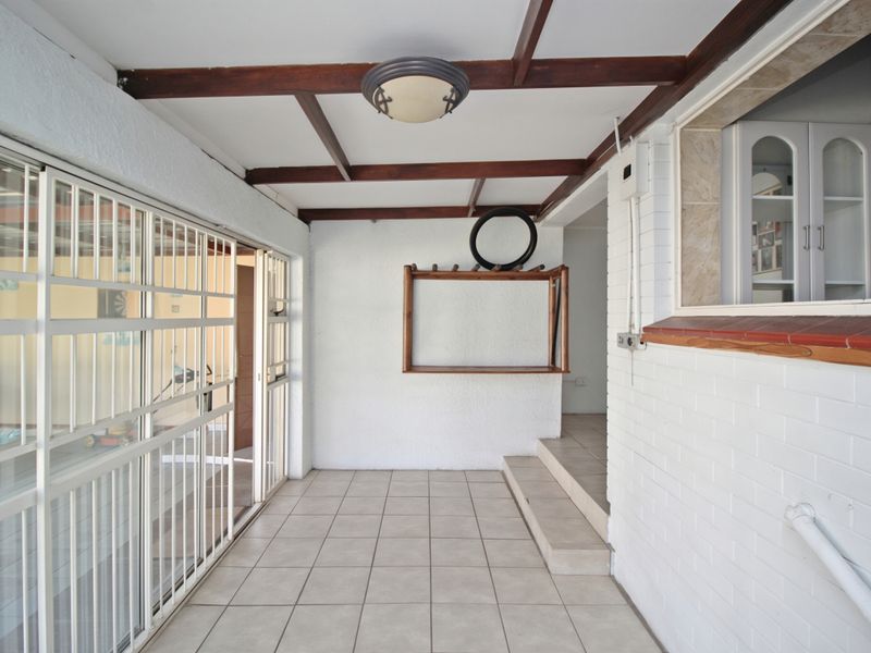 A covered patio area featuring tiled flooring, exposed timber beams, and a secure sliding gate, offering a functional outdoor transition space.