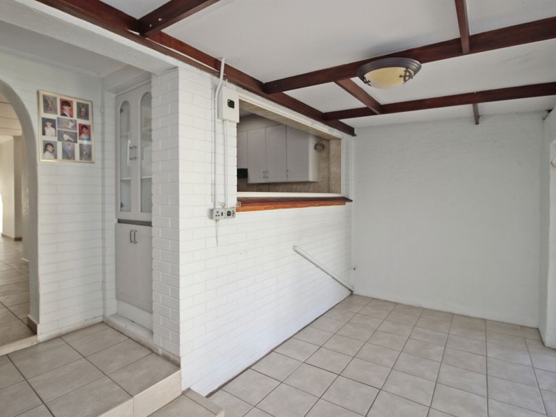 A covered patio area featuring tiled flooring, exposed timber ceiling beams, and a convenient serving hatch connecting to the kitchen space.