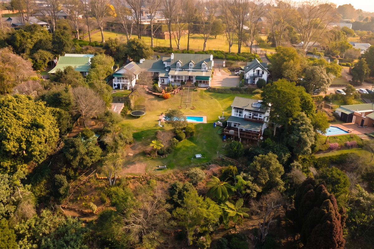 Aerial view of a large residential estate featuring multiple buildings, expansive landscaped gardens, swimming pools, and mature trees in a serene setting.
