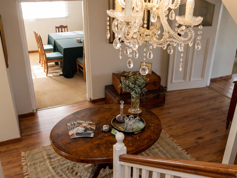 An elegant entrance hall featuring timber flooring, a grand crystal chandelier, and a timber staircase, leading through to an adjacent dining area.