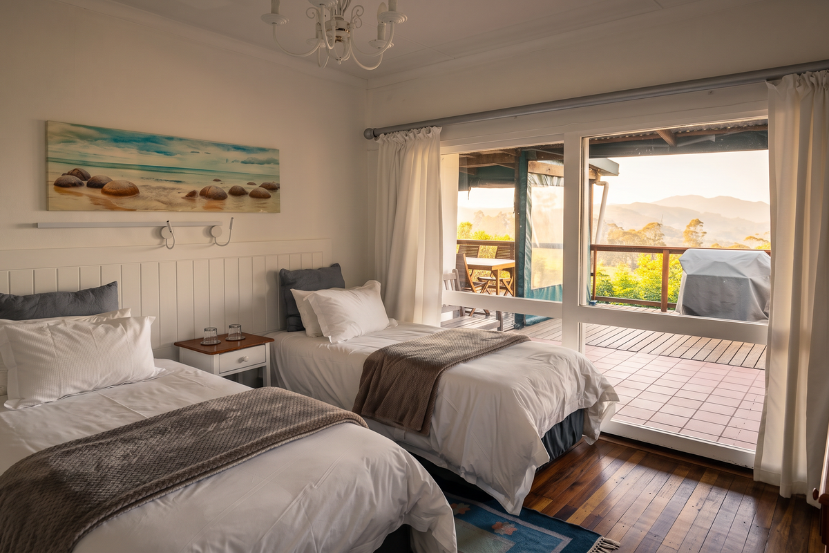 A bright bedroom featuring timber flooring and a large sliding glass door that opens onto a private balcony with scenic mountain views.