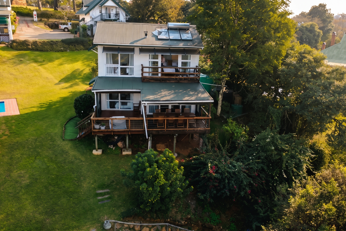 Aerial view of the rear elevation featuring a multi-level timber deck, balcony, corrugated metal roof with solar heating, and a well-maintained garden with pool.