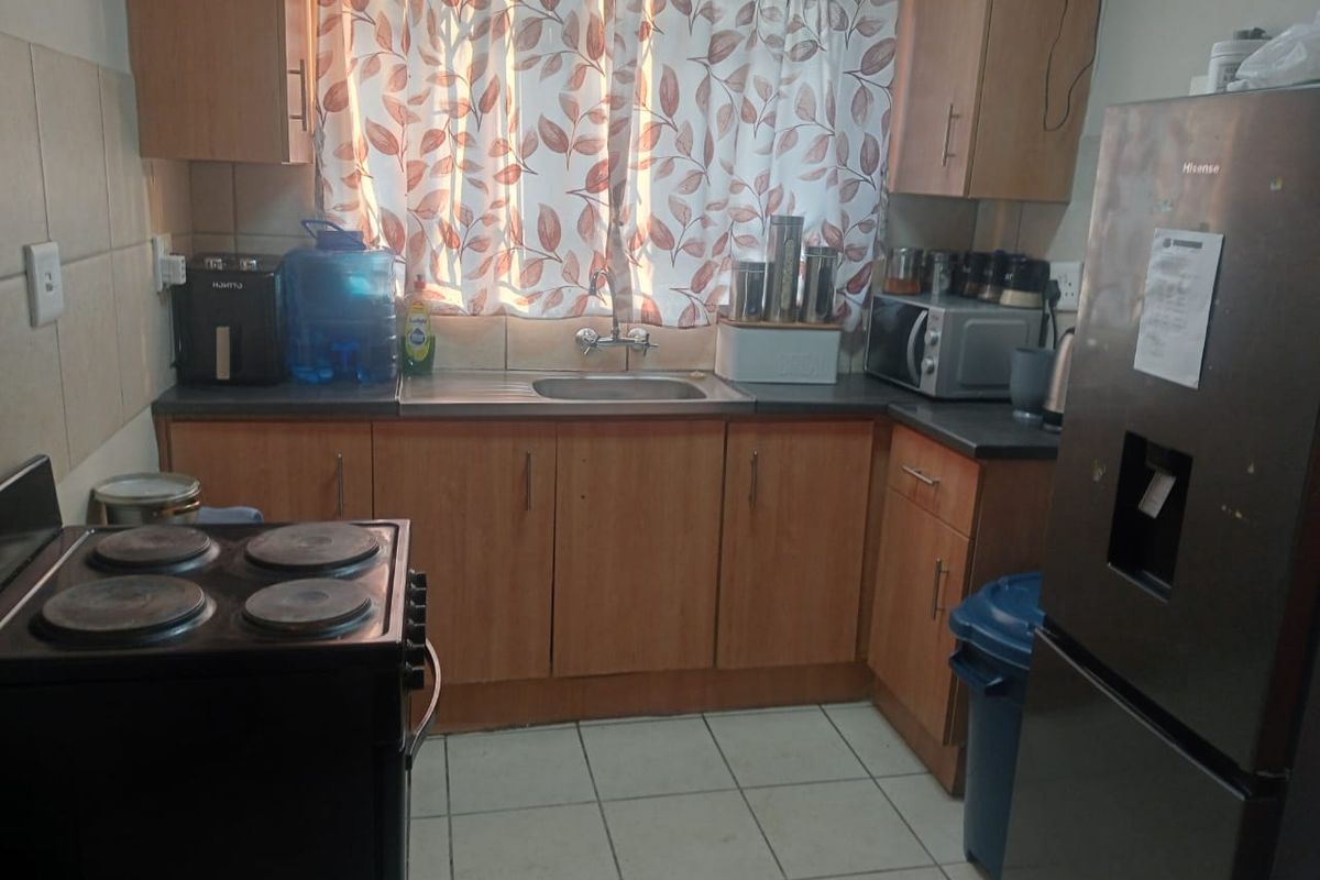 A functional kitchen featuring laminate cabinetry, a stainless steel sink, tiled backsplash, and tiled flooring, providing a practical workspace for daily meal preparation.