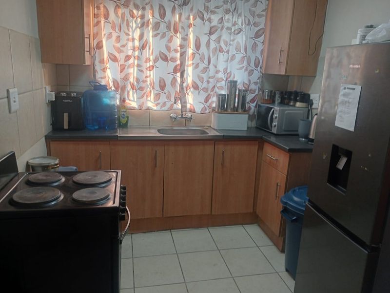 A functional kitchen featuring laminate cabinetry, a stainless steel sink, tiled backsplash, and tiled flooring, providing a practical workspace for daily meal preparation.