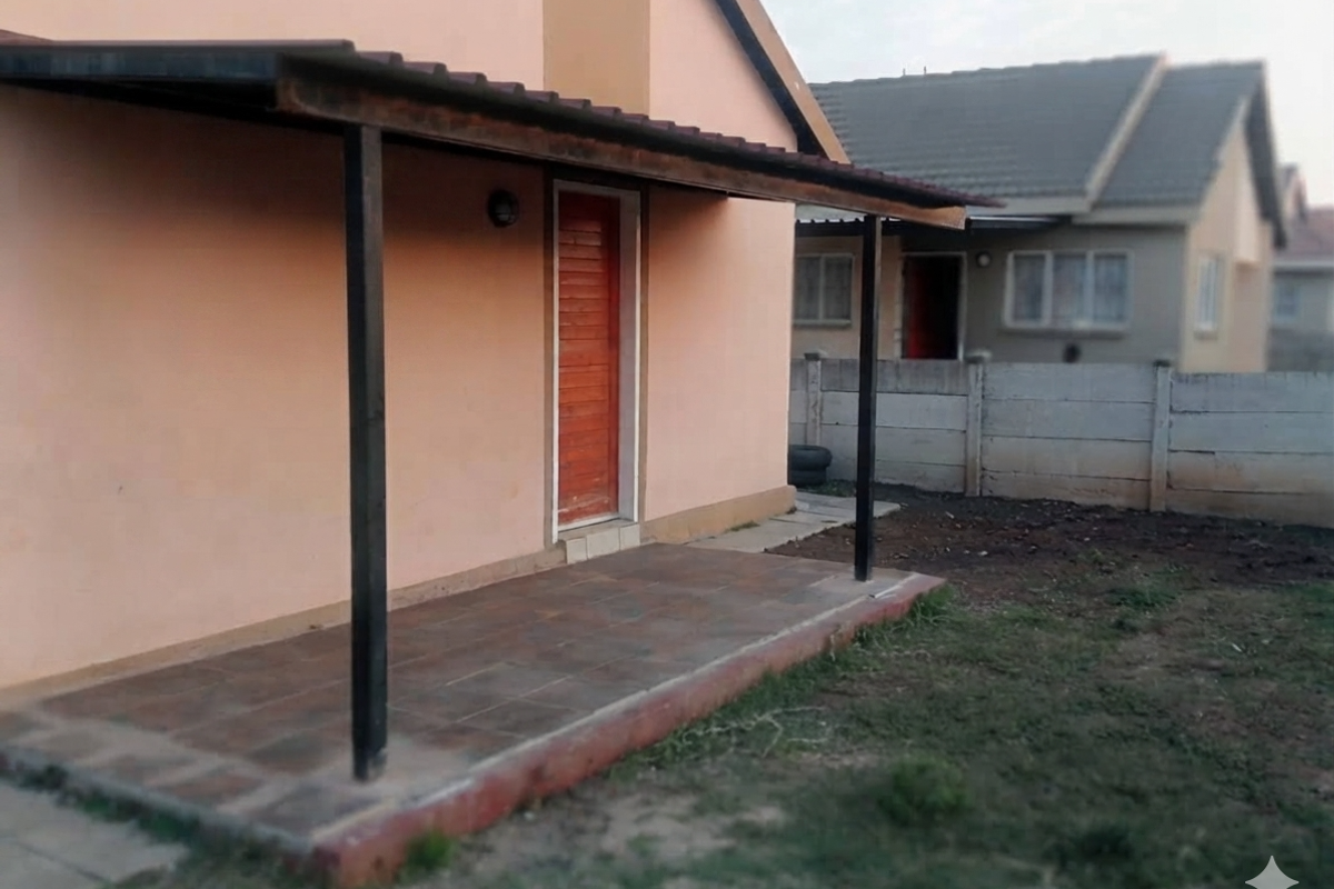 A rear exterior view of the house featuring a covered patio area with tiled flooring and a concrete boundary wall in the backyard.