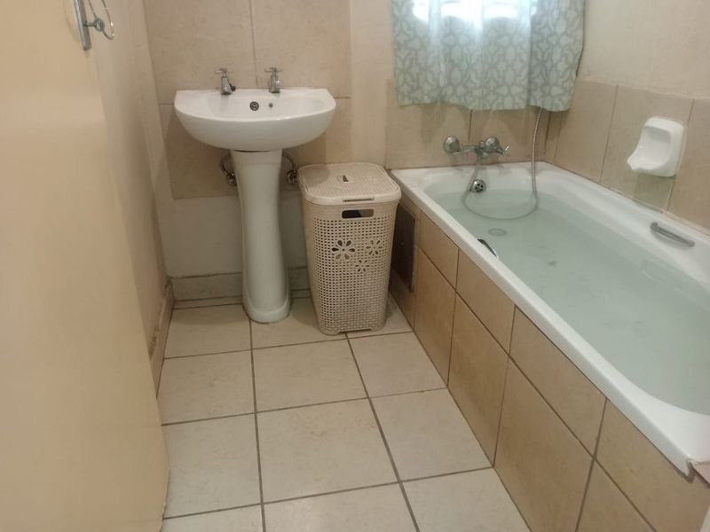 A functional bathroom featuring a pedestal basin and a tiled bathtub with wall-mounted fixtures, requiring cosmetic updates to improve its overall aesthetic appeal.