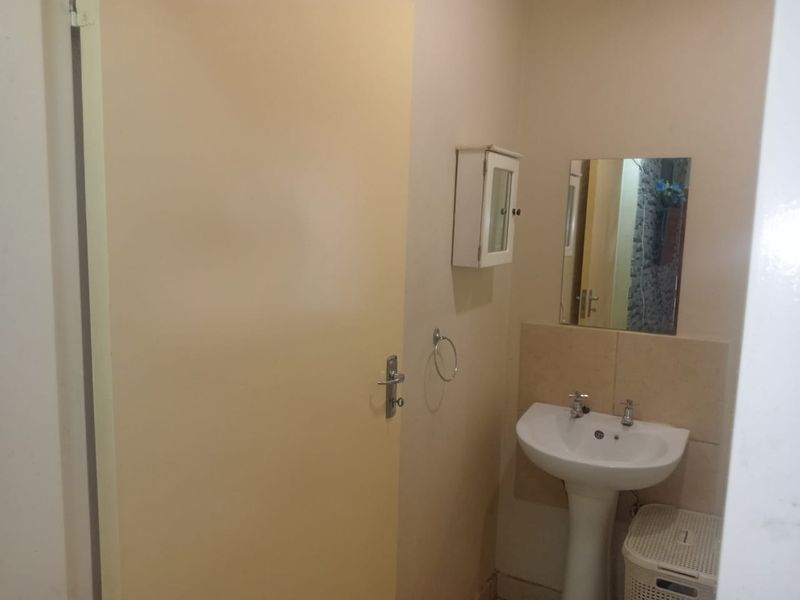 A simple guest bathroom featuring a pedestal basin, wall-mounted mirror, and storage cabinet, providing functional utility in a compact space.