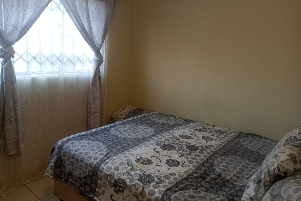 A standard bedroom featuring tiled flooring and a window fitted with a security gate.