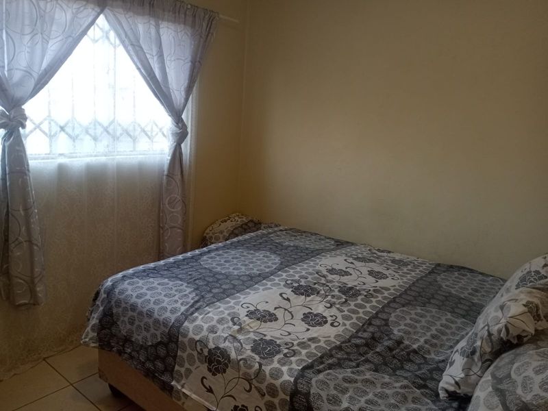 A standard bedroom featuring tiled flooring and a window fitted with a security gate.