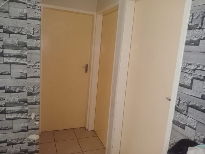 A narrow hallway featuring tiled flooring and multiple internal doors, currently showing signs of wear including peeling wallpaper.