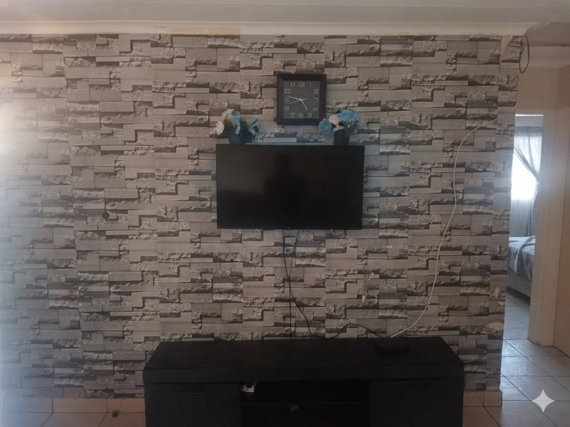 Living room area featuring stone-effect wallpaper and tiled flooring, with visible electrical cabling and dated wall finishes.