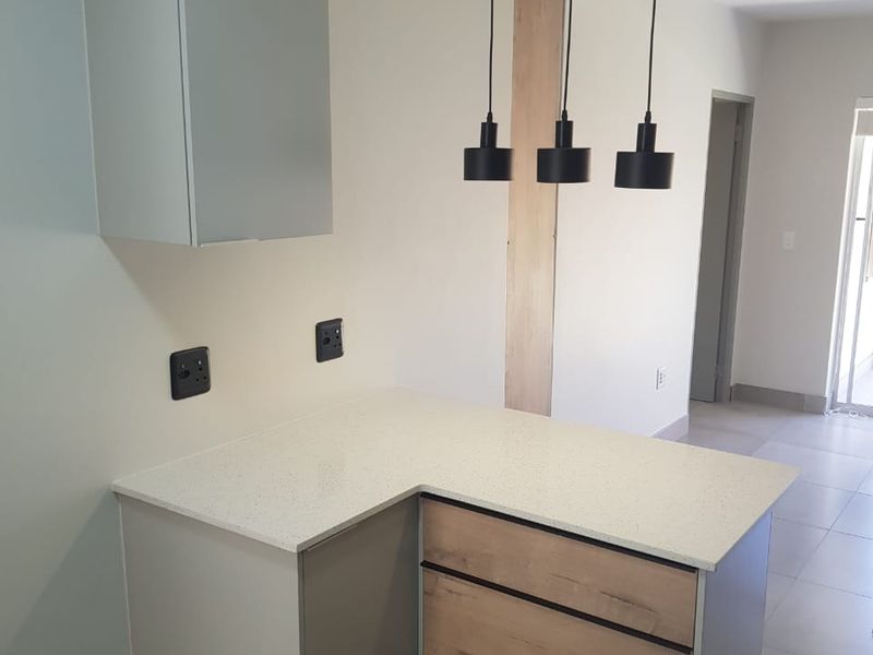 A modern kitchen area featuring a quartz countertop, built-in cabinetry with wood-grain accents, and contemporary pendant lighting in an open-plan layout.
