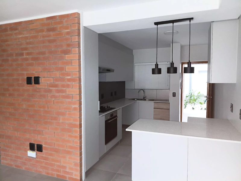 Modern open-plan kitchen featuring sleek cabinetry, stone countertops, built-in appliances, and a striking exposed brick feature wall, leading to an outdoor area.