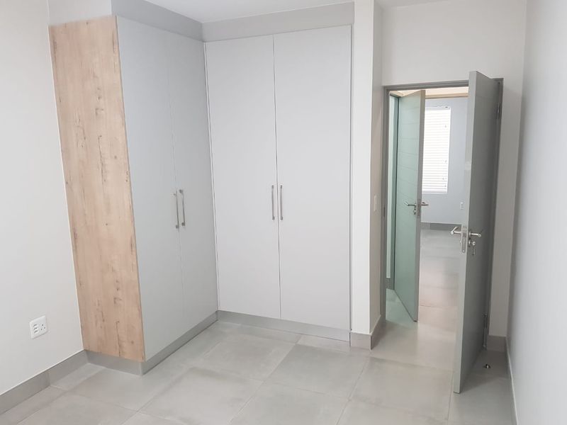 A clean, modern bedroom featuring neutral-toned built-in cupboards, large format floor tiles, and a contemporary internal door leading to an adjacent space.