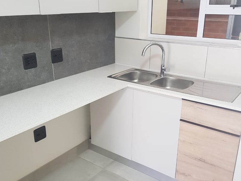 A clean and modern scullery featuring stone-look countertops, a double bowl stainless steel sink, and ample built-in cabinetry for organized storage.