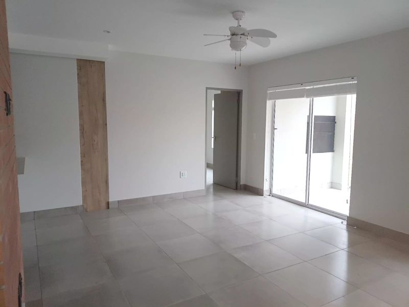 A bright, empty living area featuring neutral tiled flooring, a ceiling fan, and sliding glass doors providing access to an outdoor space.