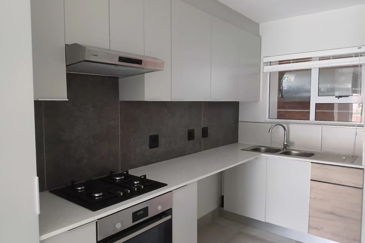 Modern kitchen featuring sleek white cabinetry, stone countertops, a gas hob, electric oven, and a double sink with a contemporary mixer tap.