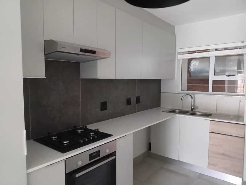 Modern kitchen featuring sleek white cabinetry, stone countertops, a gas hob, electric oven, and a double sink with a contemporary mixer tap.