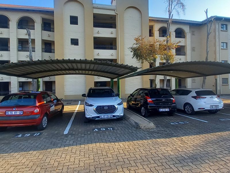 Exterior view of the apartment complex featuring a paved parking area with covered carports for residents.